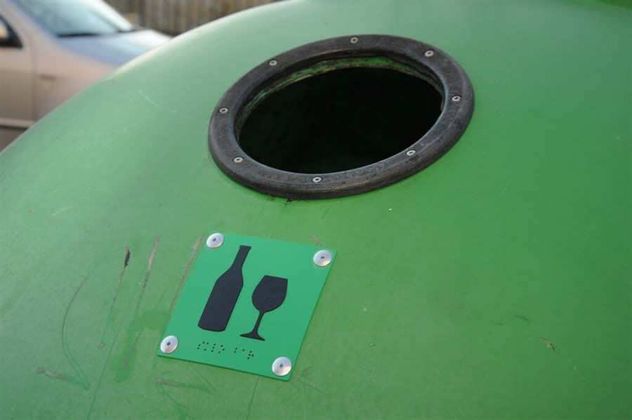 Zelený kupolovitý kontajner na sklo s kruhovým otvorom, pod ktorým sa nachádza štítok s reliéfnym označením