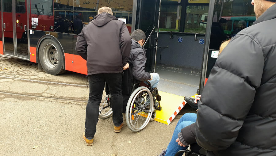 Dvaja účastníci školenia si počas praktickej časti skúšajú ako nastúpiť do spoja na invalidnom vozíku